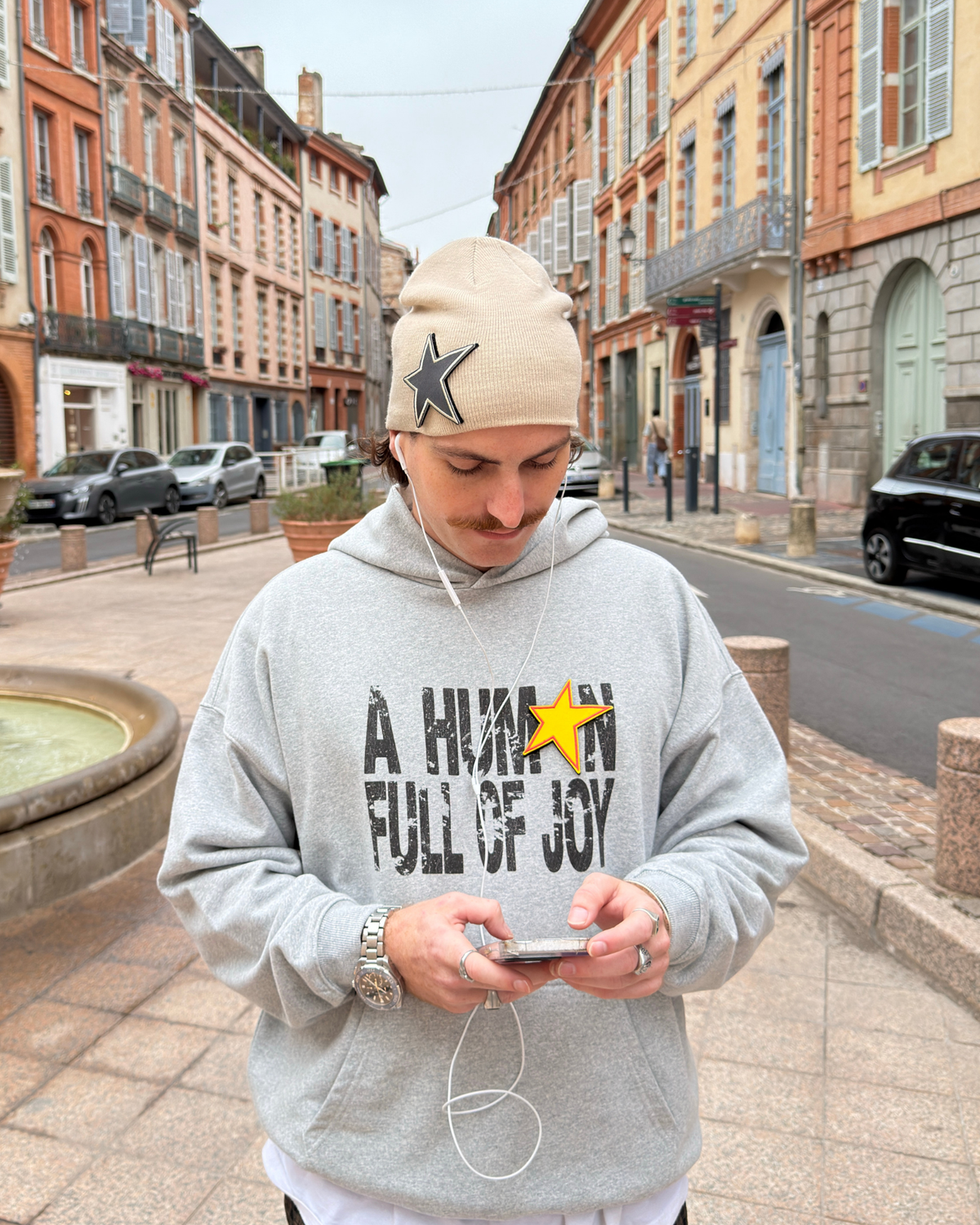 Homme portant le JOY HOODIE gris et le bonnet STAR BEANIE MUZO dans une rue de Toulouse
