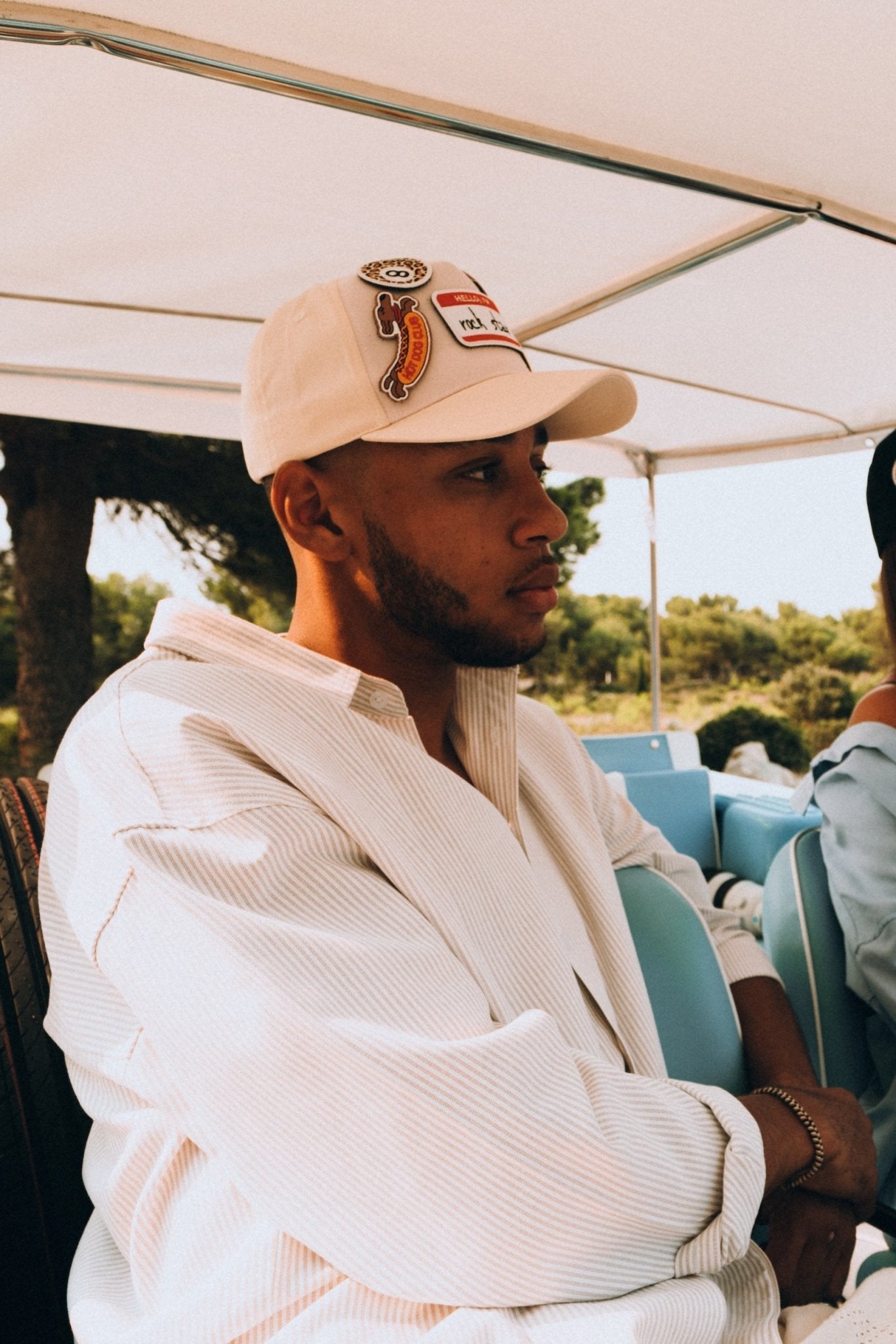 Homme portant une casquette Muzo beige personnalisée avec des patchs piment et smiley, assis dans un véhicule.