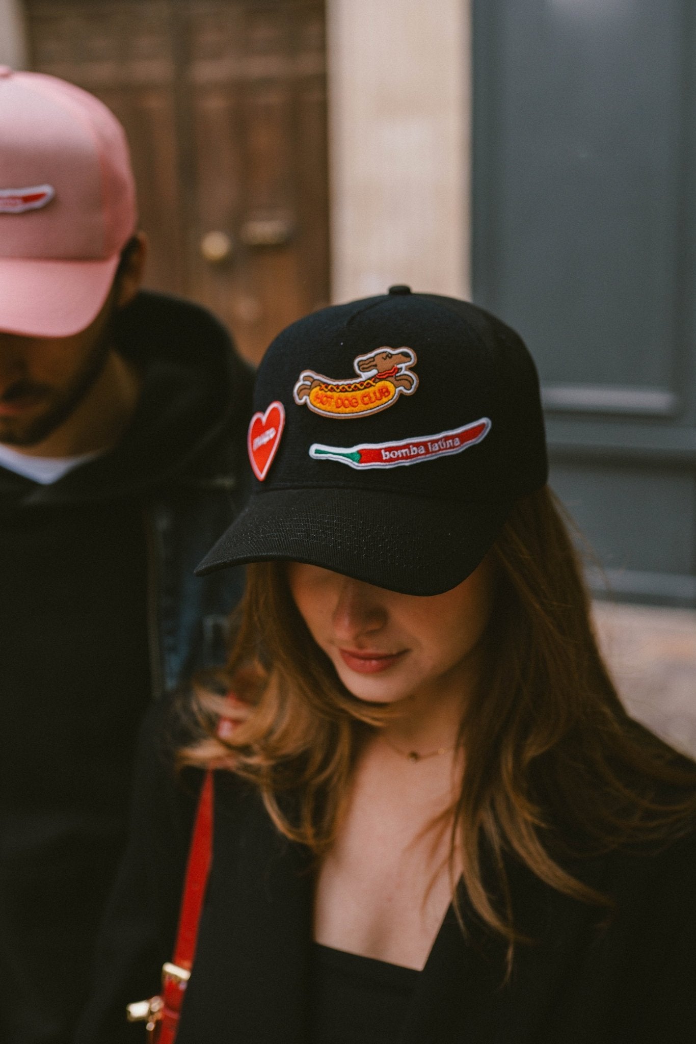 Femme portant une casquette noire Muzo personnalisable, décorée avec trois patchs scratchables : un cœur rouge, un teckel "Hot Dog Club" et un piment "Bomba Latina"
