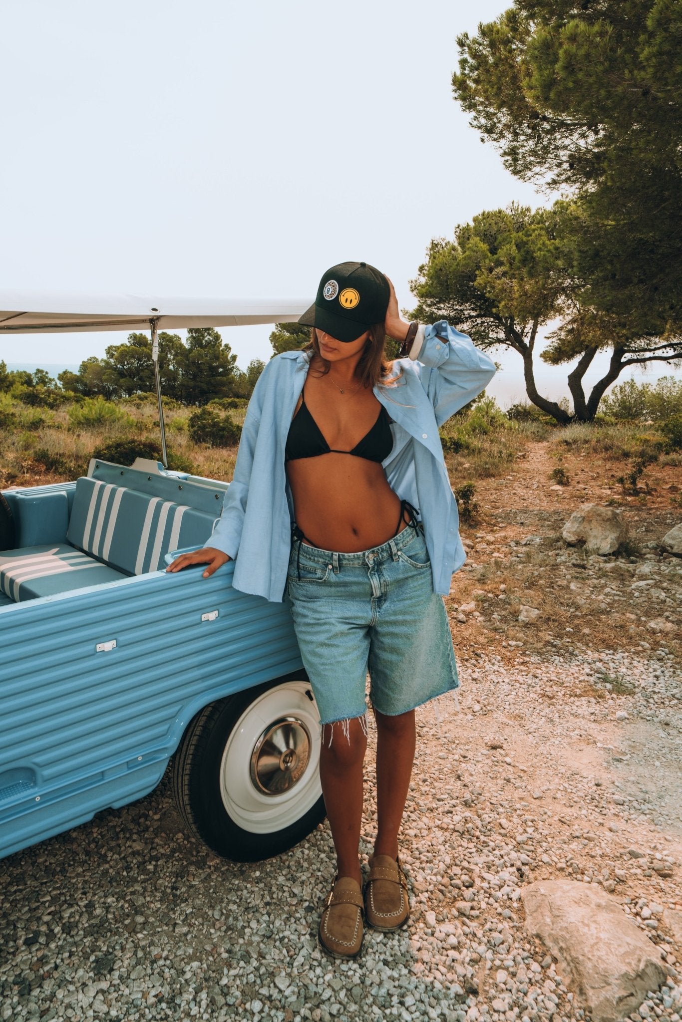 Femme portant une casquette Muzo noire personnalisée avec un assortiment de patchs colorés. Look été et stylé face à la mer.