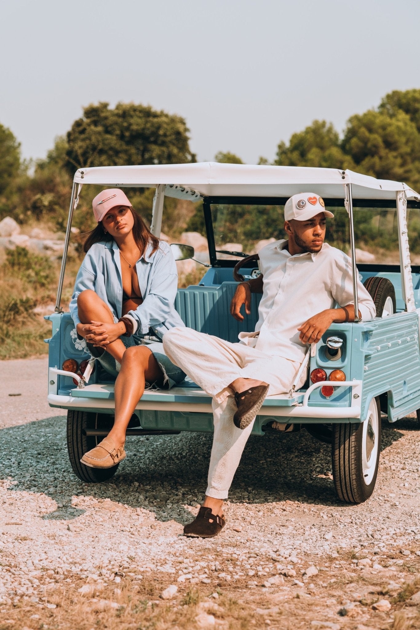 Homme et femme portant des casquettes Muzo à scratch sur une voiture vintage bleue, look streetwear décontracté pour couple.