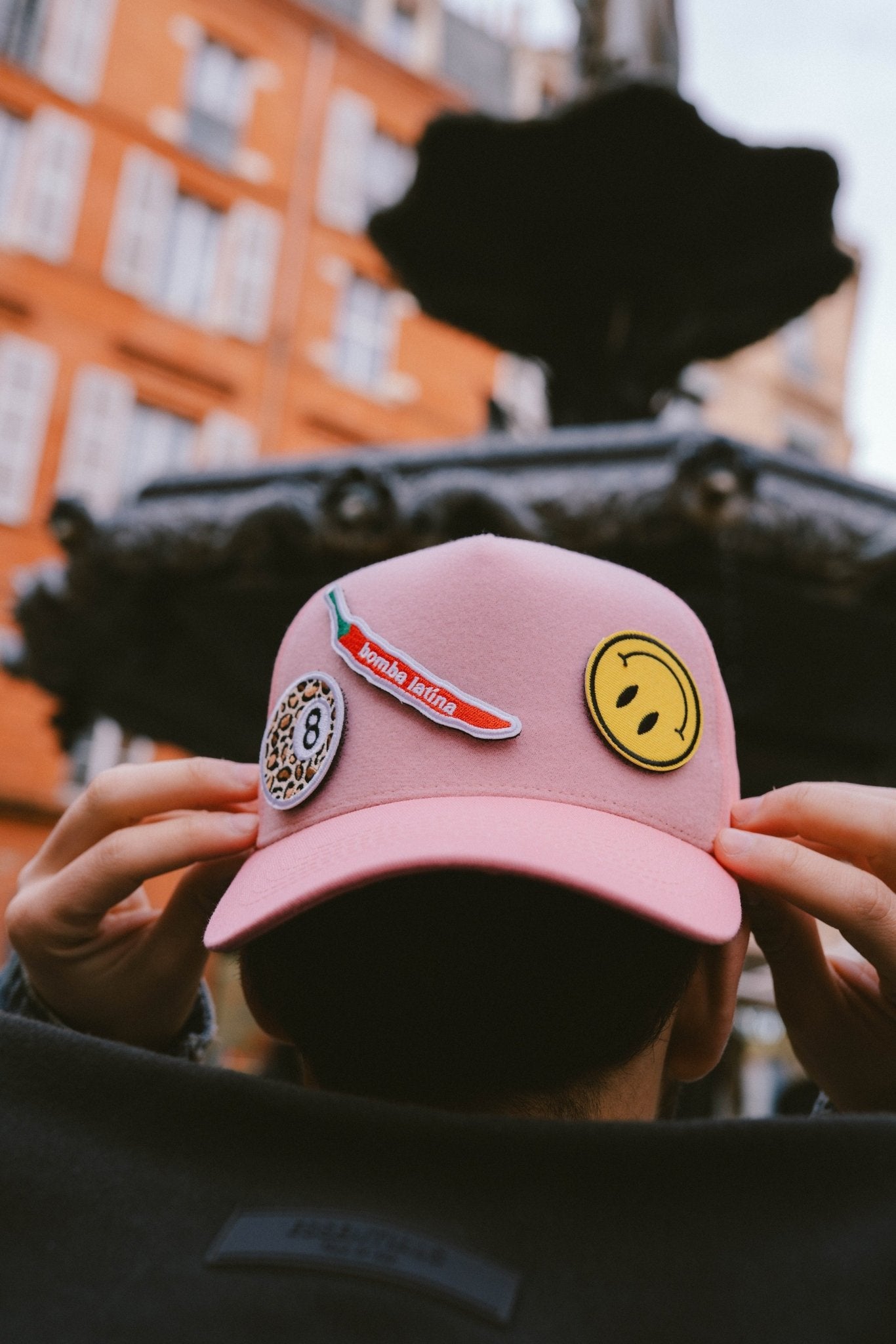 Gros plan sur une casquette rose Muzo portée, customisée avec trois patchs velcro : piment, smiley et motif léopard.
